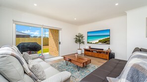 A living room with a sofa, coffee table, and a TV mounted on the wall. - Woonan - Modern and designed with families in mind (Warrnambool)