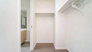 A walk-in closet with a hanging rod and a door leading to a bathroom. - Woonan - Modern and designed with families in mind (Warrnambool)