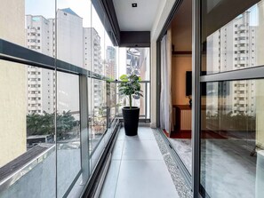 A balcony with a potted plant, glass railings, and a view of high-rise buildings. - 1 Bedroom Queen Jardins Pool Garage Metro PKS48 (São Paulo)