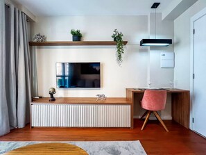 A modern living room with a flat-screen TV mounted on the wall, a wooden desk, a pink chair, and a radiator below the TV. - 1 Bedroom Queen Jardins Pool Garage Metro PKS48 (São Paulo)