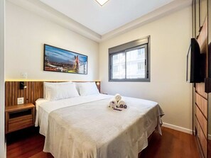 Une chambre d’hôtel avec un lit, une table de chevet, un téléviseur fixé au mur, une fenêtre donnant sur un paysage agréable et un tableau accroché au mur.