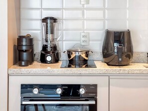 Une cuisine équipée d’une machine à café, d’un mixeur, d’une casserole sur une plaque de cuisson mobile et d’un four.