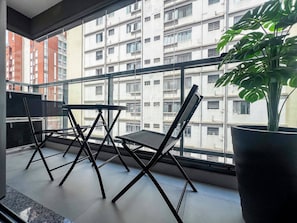 Un balcon donnant sur un immeuble à plusieurs étages, avec une plante en pot et deux chaises noires.