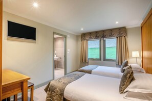 A hotel room with two beds, a desk, a television, and a bathroom visible through an open door. - The Derwent Spa (Hexham)
