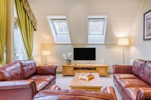 A living room with two leather sofas, a wooden coffee table, a flat-screen TV, and a small wooden side table with a vase of flowers. - The Derwent Spa (Hexham)