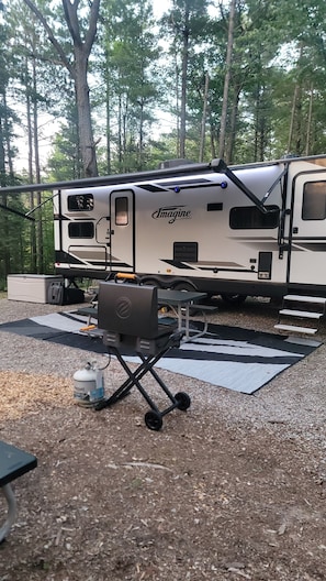 A recreational vehicle with a table and grill set up in a forested area.