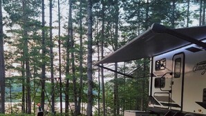 Ein Wohnmobil mit überdachter Picknickecke, Grill und Tisch mit Stühlen auf einem Kiesgrundstück.