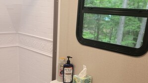 Ein kleines Badezimmer mit Dusche, Toilette und Waschbecken. Ein Fenster bietet Blick auf Bäume.