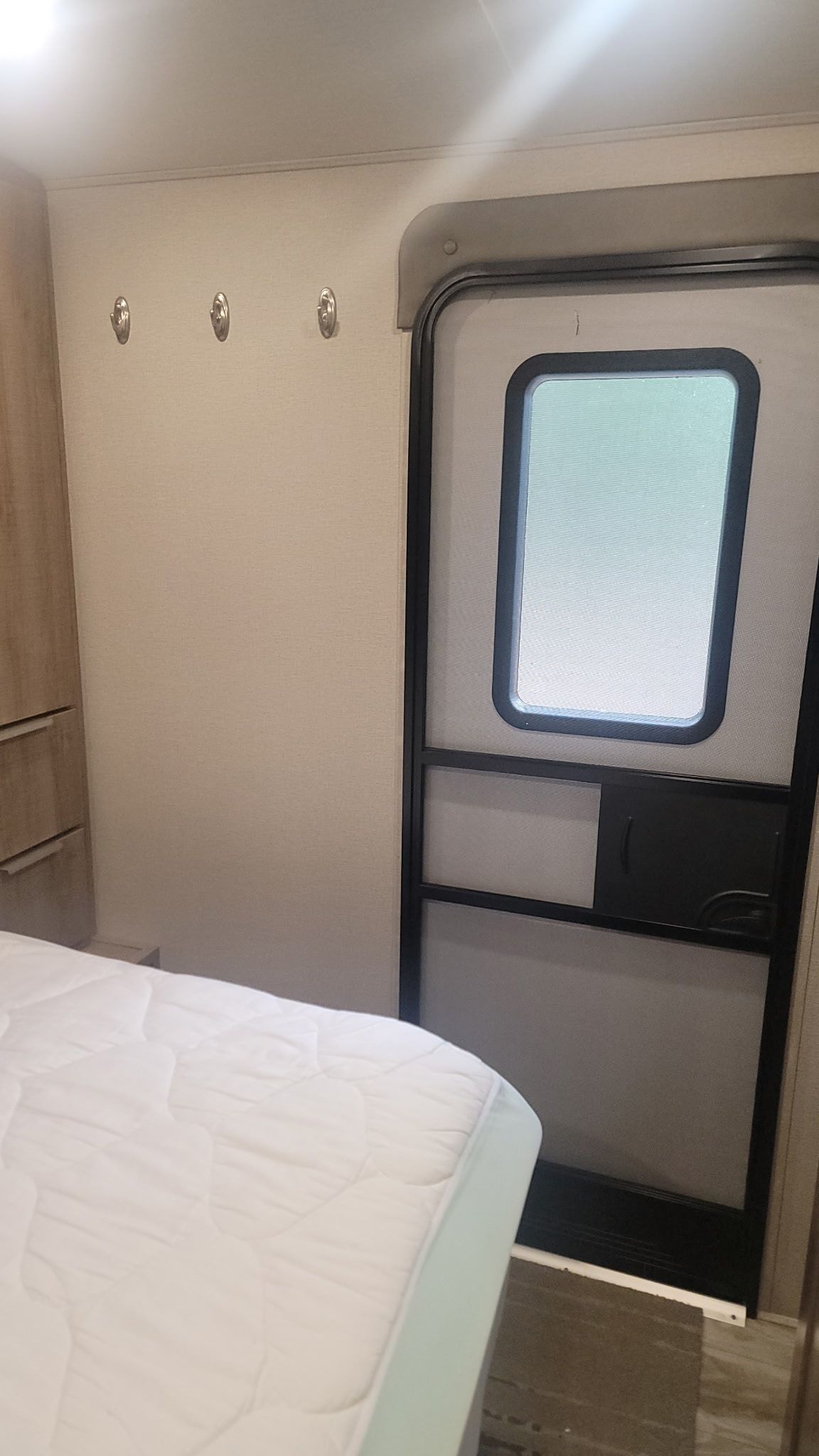 A compact RV interior with a bed, a window, and a kitchenette area.