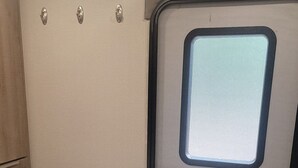 Ein kompaktes Wohnmobil-Interieur mit Bett, Fenster und einer Küchenzeile.