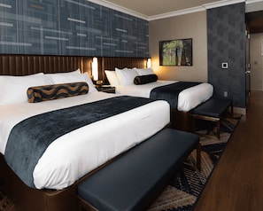 Une chambre d’hôtel avec deux lits, un banc, une table de chevet, un téléviseur fixé au mur et une moquette à motifs.