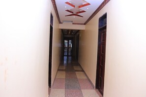 A narrow hallway with a checkered floor, a wooden door on the right, and a ceiling with a geometric design.