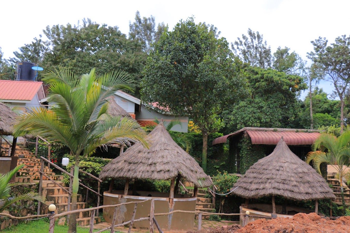 Cabanas com telhado de palha, rodeadas por vegetação e um edifício com telhado vermelho.
