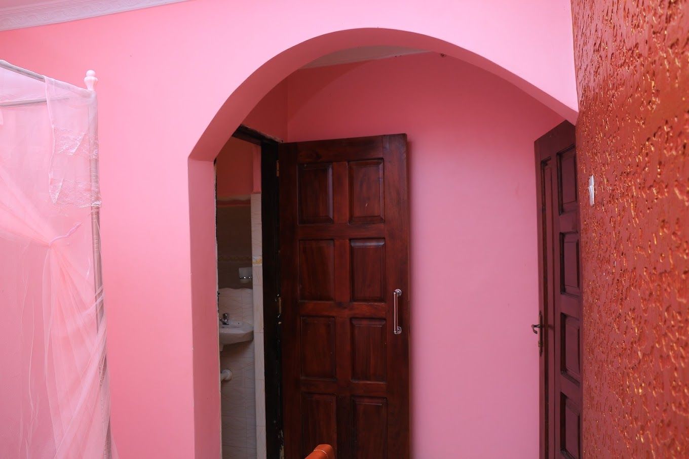 Quarto com paredes cor-de-rosa, porta de madeira e uma pequena janela.