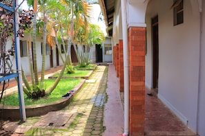 Un pasillo con piso de baldosas, una pared de ladrillo a un lado y una fila de palmeras al otro.