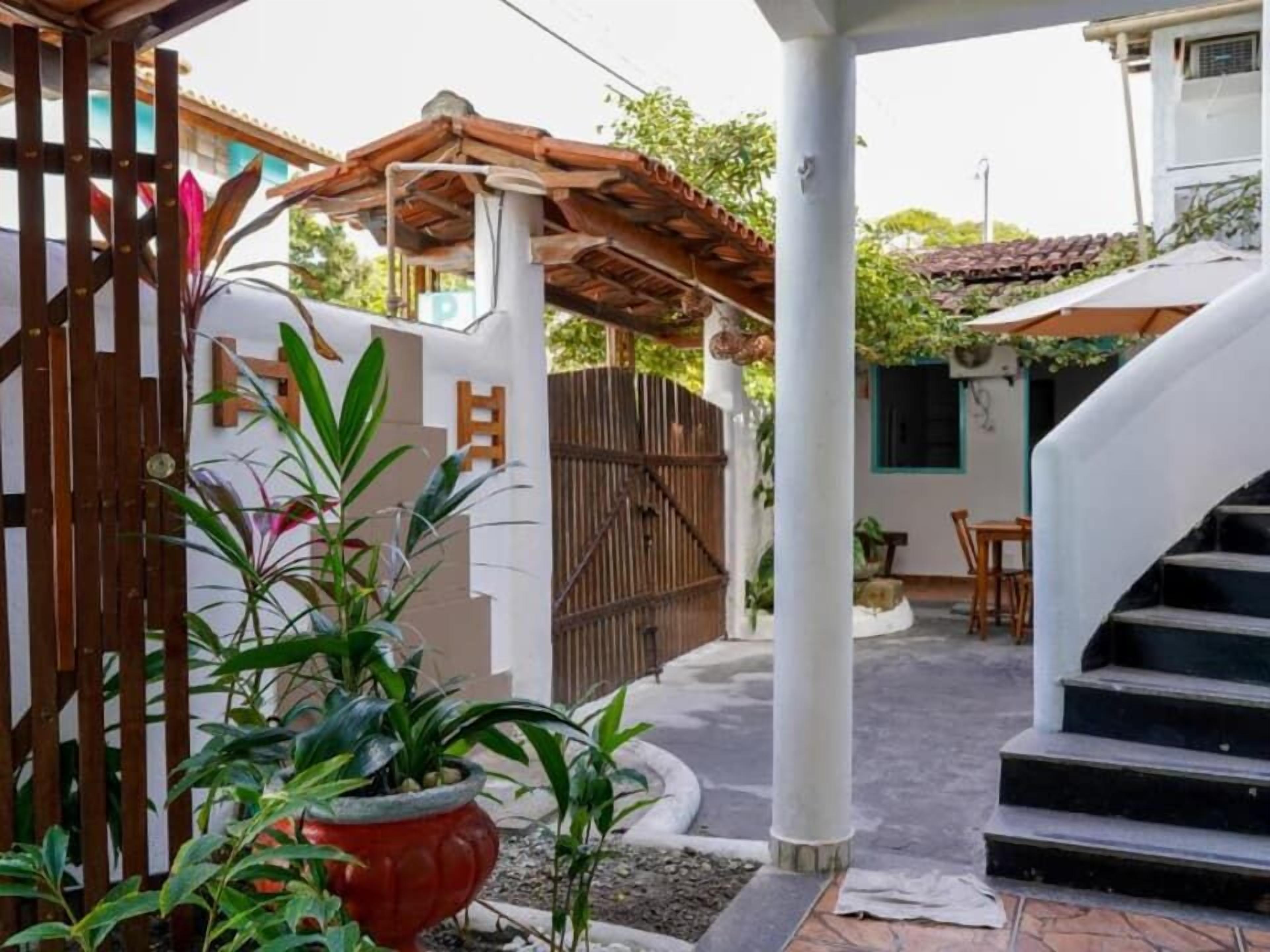 Un espacio al aire libre cubierto con una pérgola de madera, un pilar blanco y una escalera que lleva a un nivel superior.