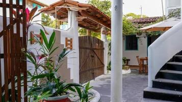 Un espacio al aire libre cubierto con una pérgola de madera, un pilar blanco y una escalera que lleva a un nivel superior.