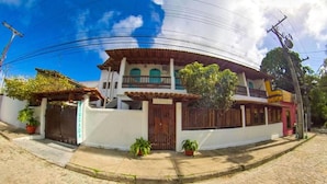 Un edificio de dos plantas con fachada blanca, balcón de madera y techo rojo.