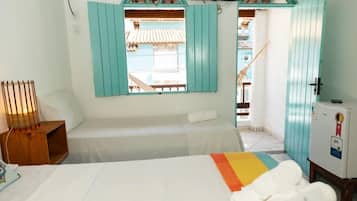 Quarto de hotel com cama, uma mesa pequena, televisão e janela com vista para um edifício.