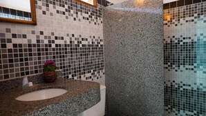 Un baño con encimera de granito, lavamanos y pared con mosaicos.