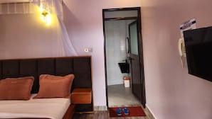 A hotel room with a bed, bedside table, and a TV mounted on the wall. - Ihunde Farm Lodge (Kiruhura)