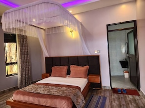 Ein modernes Schlafzimmer mit einem großen Bett, Nachttischen, einem Baldachin und Blick ins Badezimmer.