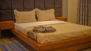 A bed with a wooden frame, two pillows, a folded blanket, and a nightstand. - Ihunde Farm Lodge (Kiruhura)