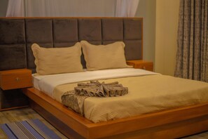 Ein Bett mit hölzernem Gestell, zwei Kissen, eine gefaltete Decke und ein Nachttisch.