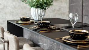A modern dining area with a marble countertop, black and gold dinnerware, and a potted plant.