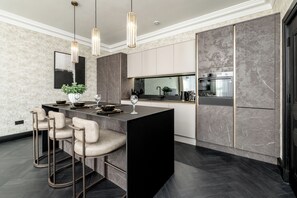 A modern kitchen with a central island, bar stools, pendant lighting, and built-in appliances. - The Onyx Residence (Edinburgh)