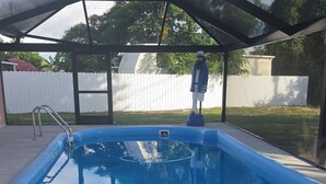 En klarblå pool med et overdækket område, omgivet af et hvidt hegn og træer.