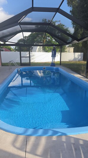 Una piscina cristallina azzurra con area coperta, circondata da un recinto bianco e alberi.