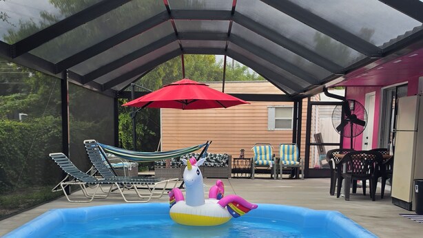 En indendørs swimmingpool med gennemsigtigt tag, omgivet af liggestole og en rød parasol.