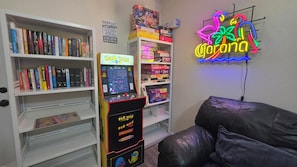 Una habitación con una máquina arcade Pac-Man, un letrero de Corona neón y estantes con juegos de mesa.