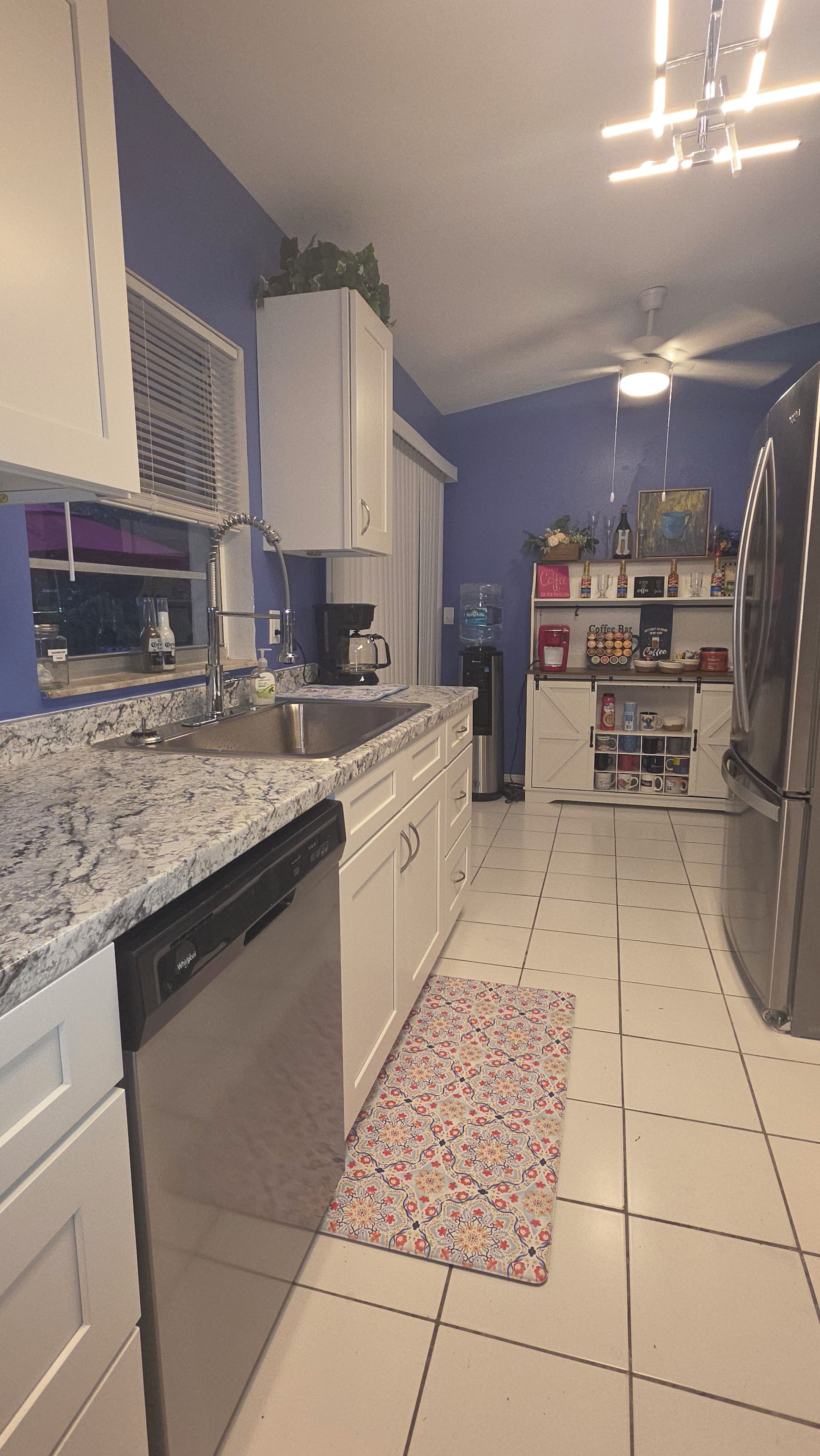 A kitchen with white cabinets, a stainless steel refrigerator, a coffee bar, and a water dispenser.