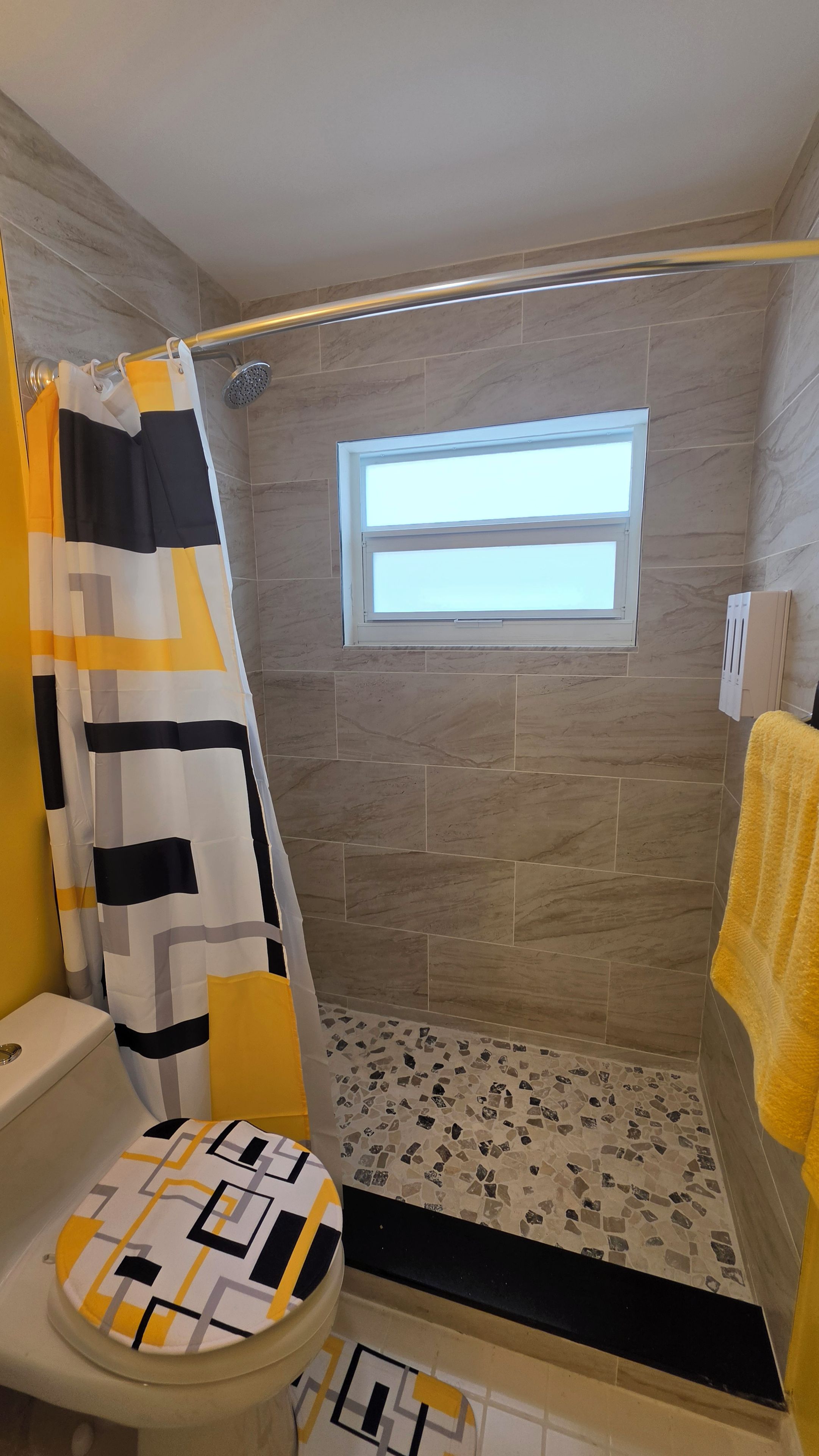 A bathroom with a shower, a toilet, and a window.