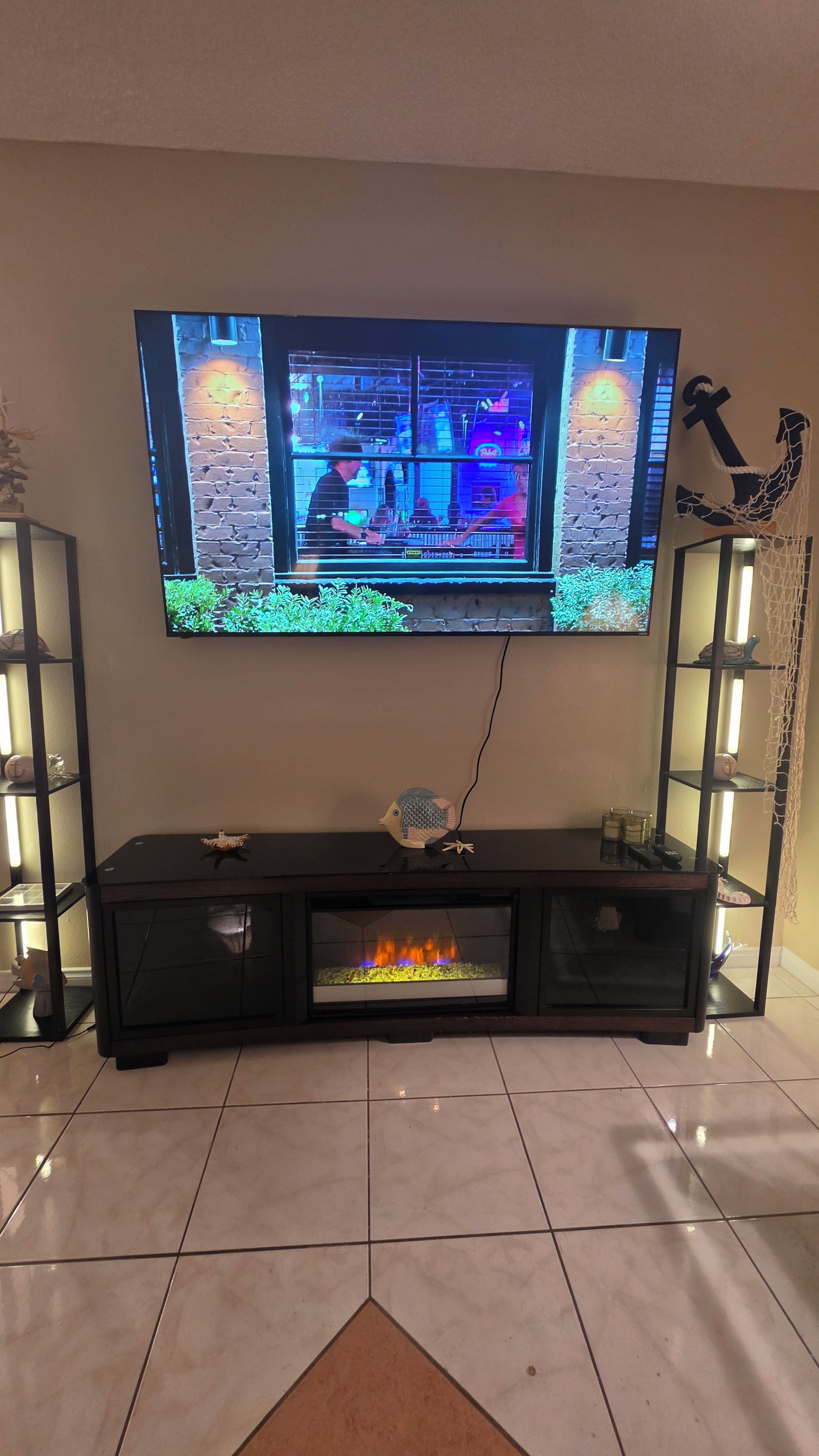 A flat-screen TV mounted on a wall above a black entertainment unit with a fireplace below.