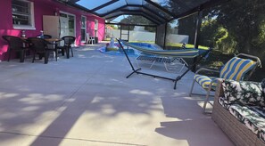 Un patio exterior con piscina, sillas de descanso y una zona de estar cubierta.