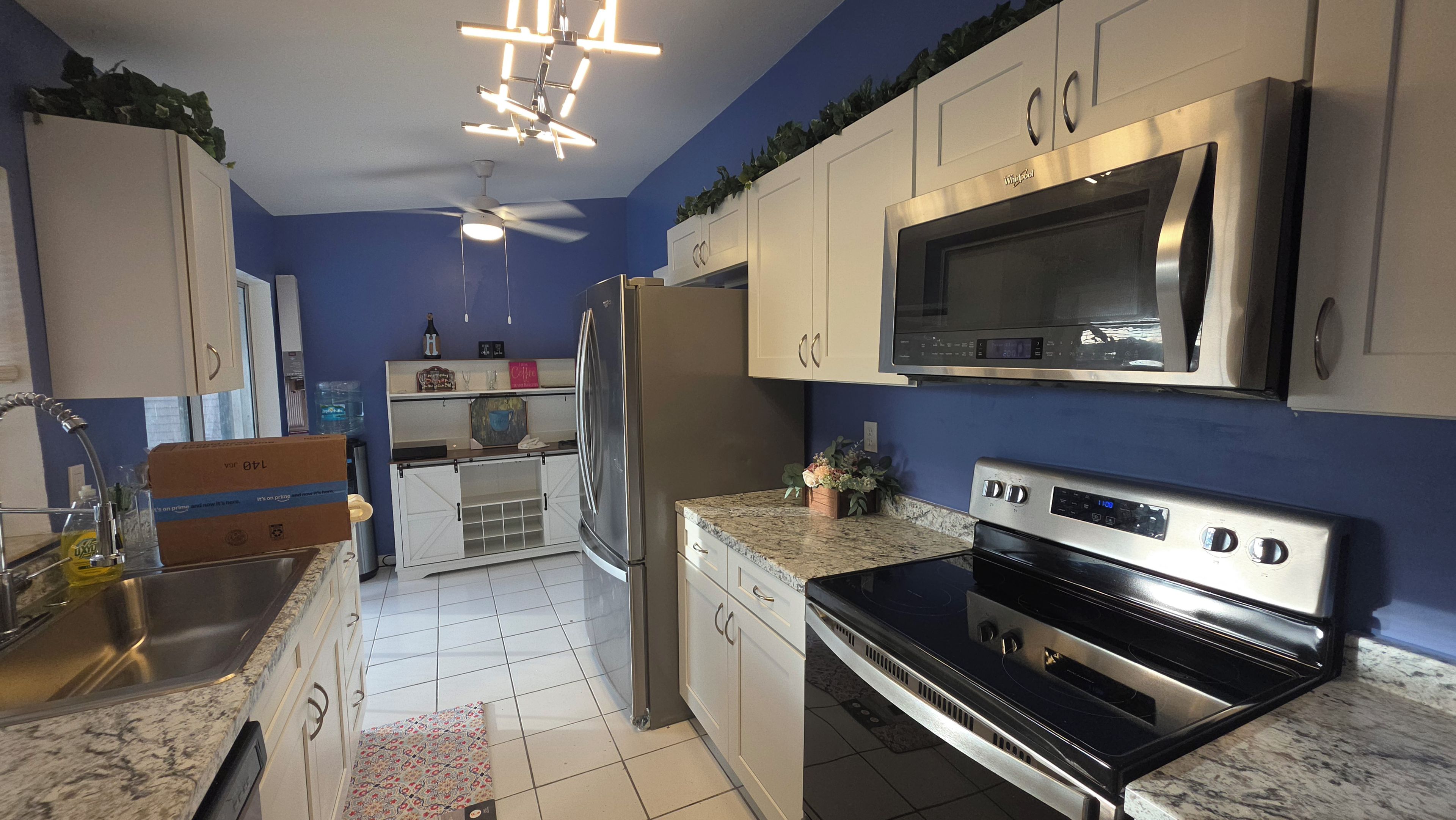 Una cocina con microondas, estufa, refrigerador y ventilador de techo.