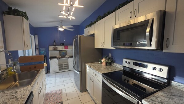 Una cocina con microondas, estufa, refrigerador y ventilador de techo.