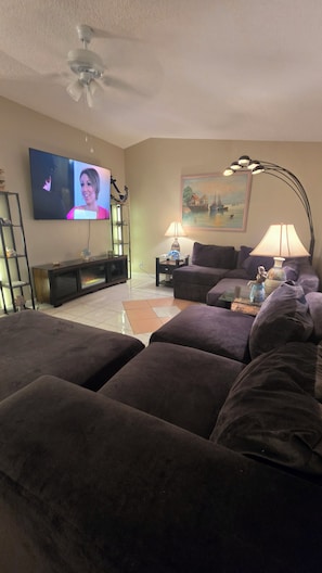 Una sala de estar con televisor, un cuadro, lámpara y ventilador de techo.