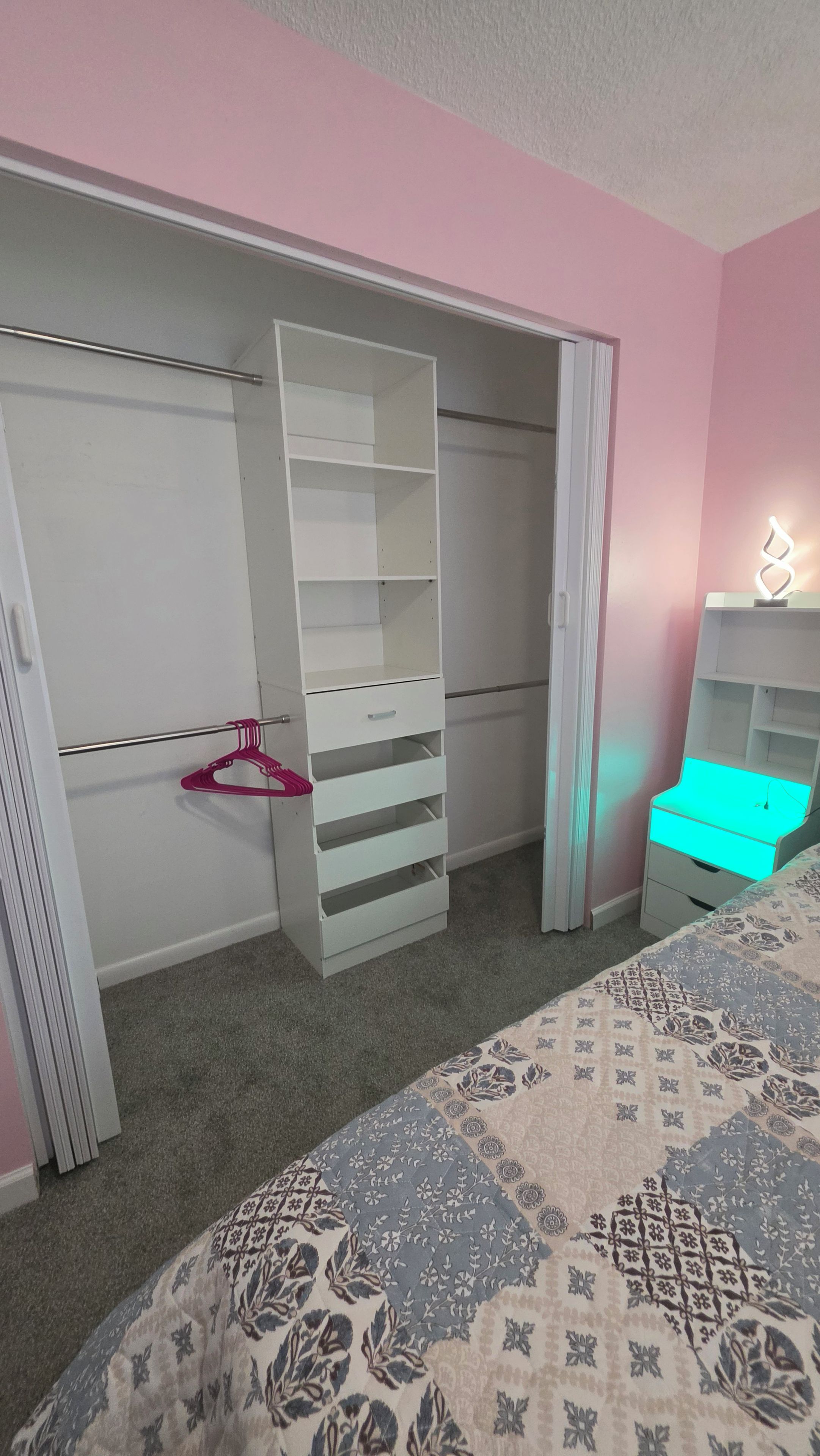 A bedroom with a bed, a closet with open doors, a dresser, and a nightstand.