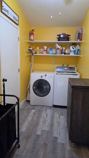 Un área de lavandería con lavadora, secadora, estantes con útiles de limpieza y extintor.