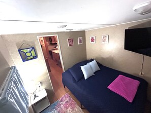 Quarto com cama, televisão e uma pequena cozinha.