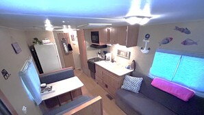 A compact RV interior with a kitchenette, a seating area, and a television. - Anchor’s Rest at Swann’s Marina
Comfort • Hot Tub • Fire Pit • Pet Friendly (Dandridge)