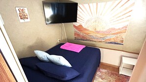 A small room with a bed, a flat-screen TV mounted on the wall, a colorful tapestry, and a small white table. - Anchor’s Rest at Swann’s Marina
Comfort • Hot Tub • Fire Pit • Pet Friendly (Dandridge)
