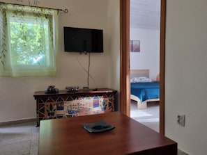 A room with a television mounted on the wall, a bed with a blue bedspread, and a wooden table with a blue cloth.