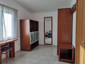 A room with a wooden desk, a chair, a wardrobe, and a mirror.