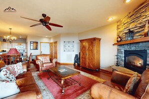 A spacious living room with a fireplace, leather sofas, a coffee table, and a ceiling fan. - Luxury 2 Bedroom Condo with Long Range Views on Sugar Mountain (Sugar Mountain)