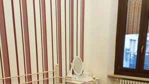 Un dormitorio con una cama, un escritorio con espejo, un radiador y una ventana con persianas.